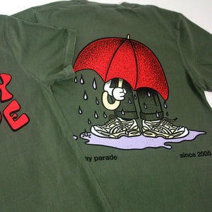 image of the back of a moss green tee shirt. tee has a full body print of a person with a big red umbrella standing in a rain puddle