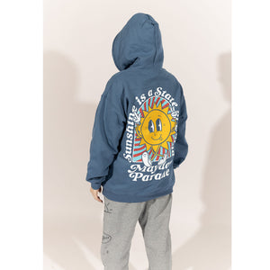 image of a woman wearing an indigo pullover hoodie. image of the back of an indigo colored pullover hoodie on a white background. the back of the hoodie has a full back print of a sun with a face, with legs and the arms in the air. arched around the sun says sunshine is a state of mind and across the bottom says mayday parade