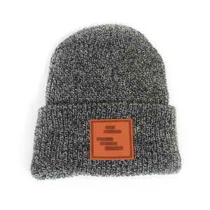 image of a black and white peppered woven winter beanie on a white background. front cuff has brown square stamped patch sewn on. five dark brown horizontal rectangles are stamped on the patch like the black lines art.