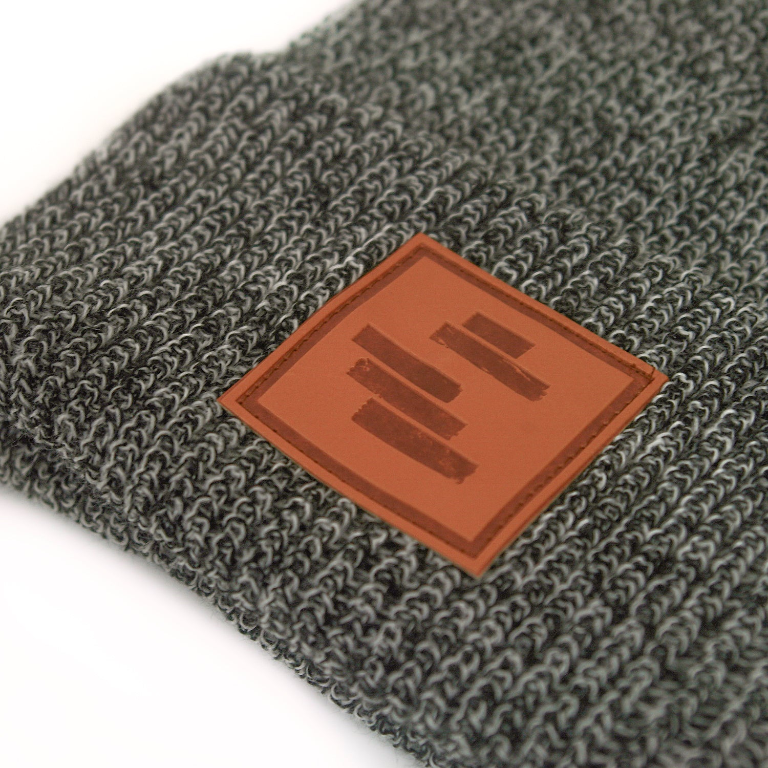 close up image of a black and white peppered woven winter beanie on a white background. front cuff has brown square stamped patch sewn on. five dark brown horizontal rectangles are stamped on the patch like the black lines art.