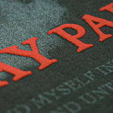 Load image into Gallery viewer, Close-up of textured black surface with large, raised red puff print letters and faint, smaller white text beneath—detail from a Mayday Parade t-shirt.
