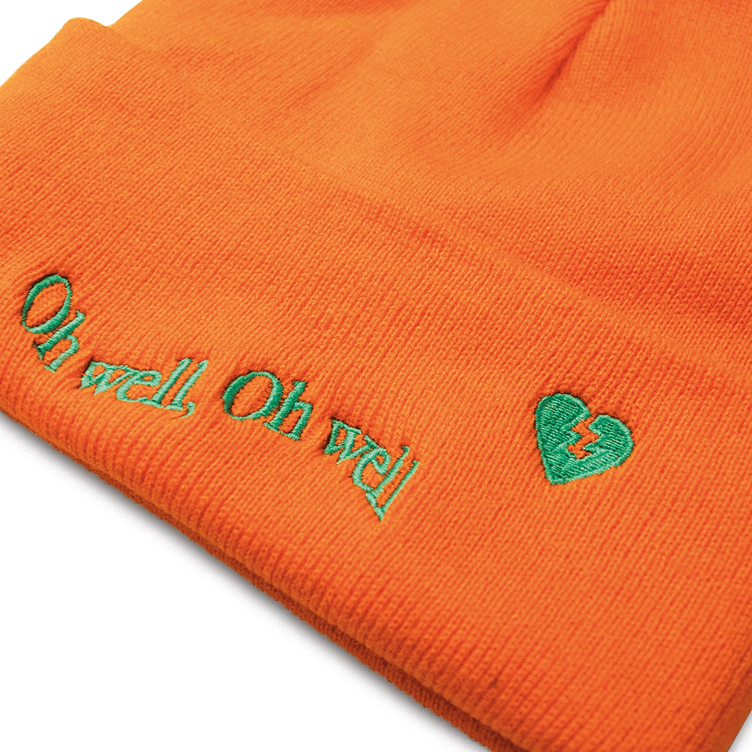close up, angled image of an orange winter beanie on a white background. front of the beanie has light green embroidery on the cuff that says oh well, oh well and a small broken heart