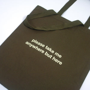 image of an army green tote bag. tote has small center print that has a small center print that says please take me anywhere but here