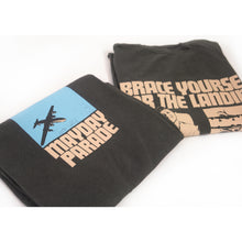 Load image into Gallery viewer, image of the front and back of a a folded pepper colored tee shirt on a white background. front is on the left and has a center chest print of a blue rectangle with an airplane. below says mayday parade. the back is on the right and has an image of a man sitting with a suitcase and a collage of airplanes. across the shoulders says brace yourself for the landing. on the bottom right says Turned upside down? dial 1 800 m l s c r s h
