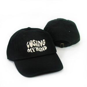 image of the front and back of a black dad hat on a white background. front of the hat is on the left and has cream embroiderd text that says losing my mind. the back of the dad hat is on the right and has black arched embroidery that says mayday parade