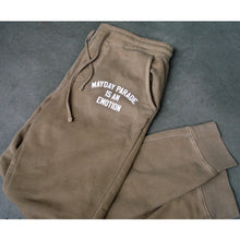 Load image into Gallery viewer, image of tan jogger sweatpants laid flat with legs folded on a concrete floor. image shows joggers drawstring laid next to the white print on top right near pocket that says mayday parade is an emotion. the legs and bottom of the joggers are shown at the bottom right of the image
