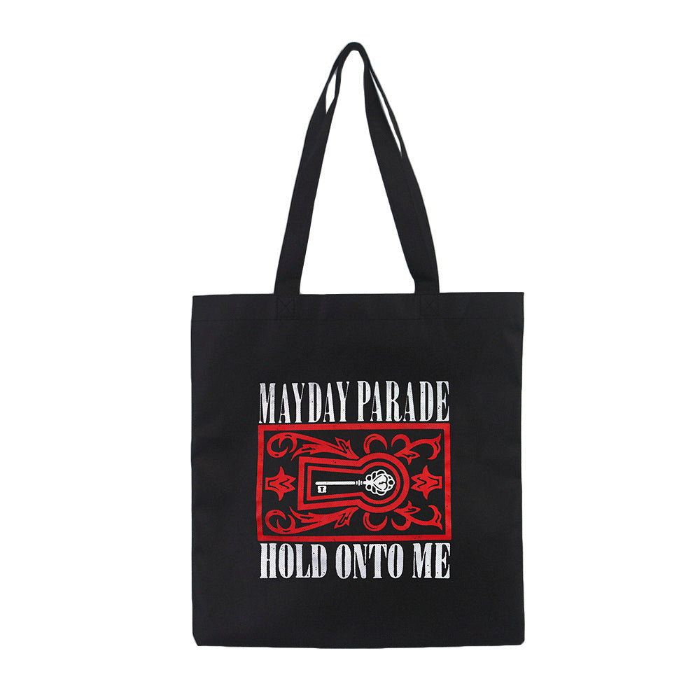 image of a black tote bag on a white background. the handles are extended up. on the front of the tote is a full print that says on top in white mayday parade, with a white key and red border around in in the center and in white below says hold onto me
