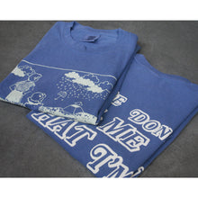 Load image into Gallery viewer, image of the front and back of a blue tee shirt folded and laid on a concrete floor. image of the front and back of a blue tee shirt on a white background. front is on the left and has an white print of a rectangle with two people staring out from to rain clouds and and umbrella. the back is on the right and says please don&#39;t tell me that I&#39;m dreaming
