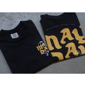 image of front and back of a black tee shirt folded and laid on a concrete floor. the front of the tee is on the left and has a grey size tag on the inside neck and a small chest print on the right in yellow and white print. the back of the tee is on the right and shows a full size print in yellow that says may day
