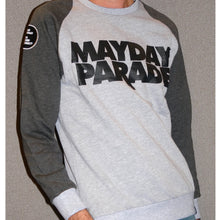 Load image into Gallery viewer, image from the neck down of a man in front of a grey background wearing a crewneck sweatshirt. the sleeves are a dark heather grey, and the chest/body is light heather grey. front chest of crewneck says stacked in black mayday parade. circle black patch with white rectangles is on the left sleeve
