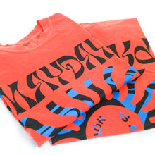Load image into Gallery viewer, image of the front and back of a salmon colored tee shirt folded and stacked on a white background. front of tee is on the left and has a full body print. at the top says mayday and the bottom says parade. in the center is a blue sun shape and inside says is an emotion. the back of the tee is on the right and has the same print as the front of the tee.
